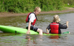 Boys Playing the in the water with kayaks wearing buoyancy aids